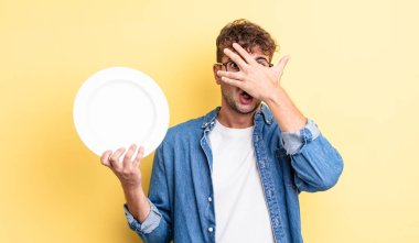 Genç, yakışıklı adam şok olmuş, korkmuş ya da korkmuş görünüyor. boş tabak kavramı