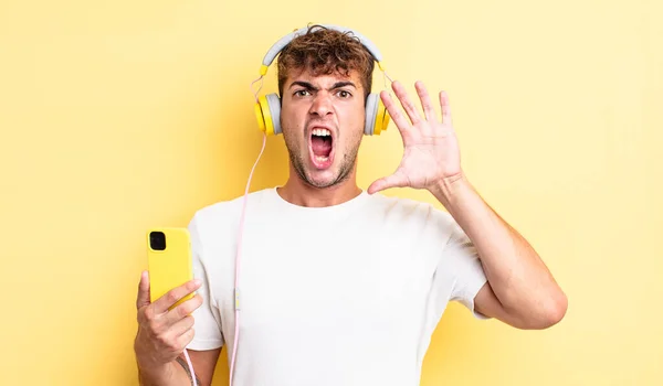 若いハンサムな男が手を上げて叫んでる ヘッドフォンとスマートフォンのコンセプト — ストック写真