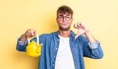 Genç yakışıklı adam kendini kötü hissediyor, başparmaklarını gösteriyor. Çaydanlık konsepti.