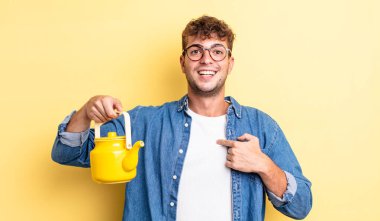 Genç yakışıklı adam kendini mutlu hissediyor ve heyecanlı bir çaydanlık konseptiyle kendini işaret ediyor.