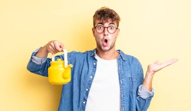 Genç yakışıklı adam şaşırmış ve şok olmuş görünüyor, çenesi düşmüş bir nesne tutuyordu. Çaydanlık konsepti.