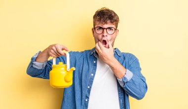 Ağzı ve gözleri sonuna kadar açık ve eli çenesinde genç yakışıklı bir adam. Çaydanlık konsepti.