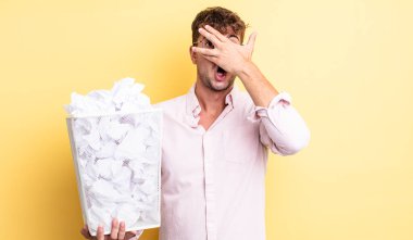Genç, yakışıklı adam şok olmuş, korkmuş ya da korkmuş görünüyor. kağıt toplar çöp konsepti