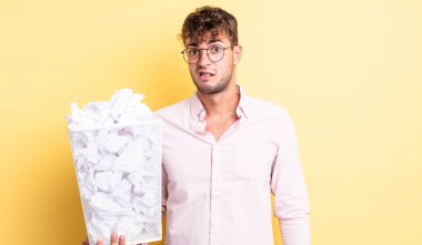 Genç yakışıklı adam şaşkın ve şaşkın hissediyor. kağıt toplar çöp konsepti
