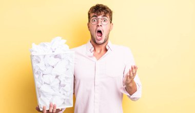 Genç ve yakışıklı bir adam şok olmuş ve şaşırmış hissediyor. kağıt toplar çöp konsepti