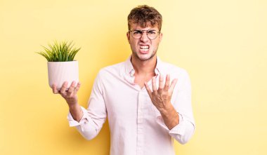 Genç ve yakışıklı bir adam sinirli, sinirli ve sinirli görünüyor. dekoratif bitki konsepti