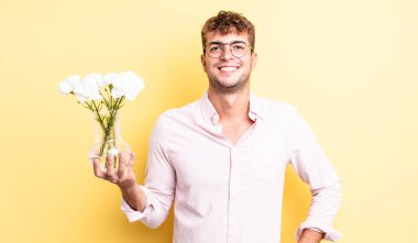Genç yakışıklı adam mutlu bir şekilde gülümsüyor, eli kalçasında ve kendinden emin. çiçek konsepti