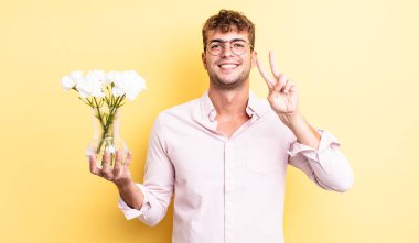 Genç yakışıklı adam gülümsüyor ve mutlu görünüyor, zafer ya da barış işareti yapıyor. çiçek konsepti