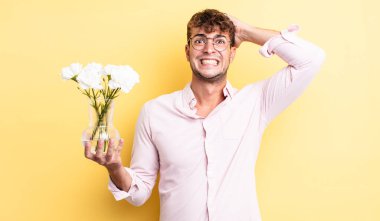 Genç ve yakışıklı bir adam stresli, endişeli ya da korkmuş hissediyor. Elleri başının üstünde. çiçek konsepti
