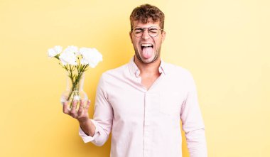 Genç, yakışıklı, neşeli ve asi tavırlı, şaka yapan ve dilini dışarı çıkaran bir adam. çiçek konsepti