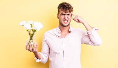Genç yakışıklı adam kafası karışık ve şaşkın hissediyor, deli olduğunu gösteriyor. çiçek konsepti