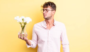 Genç ve yakışıklı bir adam üzgün, üzgün ya da kızgın hissediyor ve yan tarafa bakıyor. çiçek konsepti