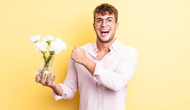 Genç yakışıklı adam kendini mutlu hissediyor ve bir meydan okumayla yüzleşiyor ya da kutluyor. çiçek konsepti