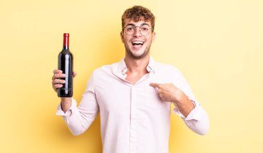 Genç ve yakışıklı bir adam mutlu hissediyor ve heyecanla kendini işaret ediyor. şarap şişesi konsepti