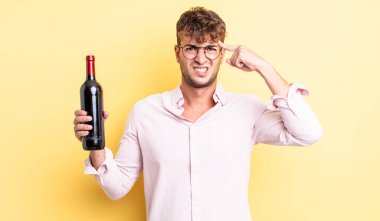 Genç yakışıklı adam kafası karışık ve şaşkın hissediyor, deli olduğunu gösteriyor. şarap şişesi konsepti