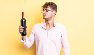 Genç ve yakışıklı bir adam üzgün, üzgün ya da kızgın hissediyor ve yan tarafa bakıyor. şarap şişesi konsepti