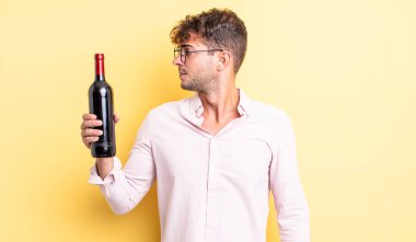 Profilde genç yakışıklı bir adam hayal kuruyor, hayal kuruyor ya da hayal kuruyor. şarap şişesi konsepti