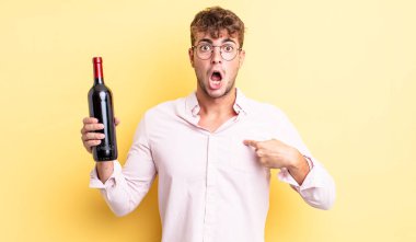 Şok olmuş ve ağzı açık, kendini işaret eden genç ve yakışıklı bir adam. şarap şişesi konsepti