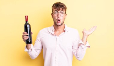 Genç, yakışıklı adam şaşırmış ve şok olmuş görünüyor. Çenesi düşmüş, elinde bir nesne var. şarap şişesi konsepti