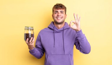 Genç yakışıklı adam kendini mutlu hissediyor, iyi bir jestle onaylıyor. kahve çekirdeği konsepti