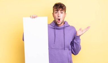 Genç, yakışıklı adam şaşırmış ve şok olmuş görünüyor. Çenesi düşmüş, elinde bir nesne var. boşluk konseptini kopyala