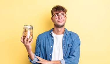 Genç yakışıklı adam omuz silkiyor, kafası karışık ve kararsız. kurabiye şişesi konsepti