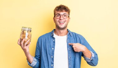 Genç ve yakışıklı bir adam mutlu hissediyor ve heyecanla kendini işaret ediyor. kurabiye şişesi konsepti