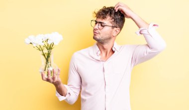Genç yakışıklı adam mutlu bir şekilde gülümsüyor ve hayal kuruyor ya da şüphe ediyor. çiçek konsepti