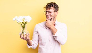 Genç ve yakışıklı bir adam mutlu ve kendinden emin bir ifadeyle gülümsüyor, elleri çenesinde. çiçek konsepti