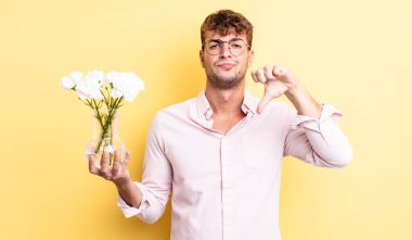 Genç ve yakışıklı bir adam kendini kötü hissediyor, baş parmağını kaldırıyor. çiçek konsepti