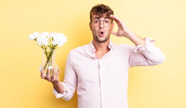 Genç yakışıklı adam mutlu, şaşkın ve şaşırmış görünüyor. çiçek konsepti