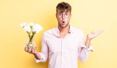 Genç, yakışıklı adam şaşırmış ve şok olmuş görünüyor. Çenesi düşmüş, elinde bir nesne var. çiçek konsepti