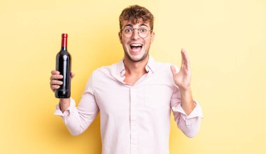 Genç yakışıklı adam kendini mutlu hissediyor ve inanılmaz bir şeye hayret ediyor. şarap şişesi konsepti