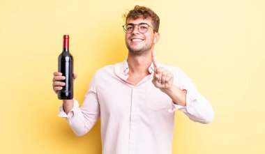 Genç yakışıklı adam gururla gülümsüyor ve kendinden emin bir numara oluyor. şarap şişesi konsepti