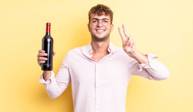 Genç yakışıklı adam gülümsüyor ve arkadaş canlısı görünüyor, iki numarayı gösteriyor. şarap şişesi konsepti