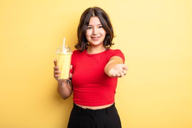 Genç ve güzel bir kadın arkadaşça gülümsüyor ve bir konsept sunuyor. Milkshake konsepti