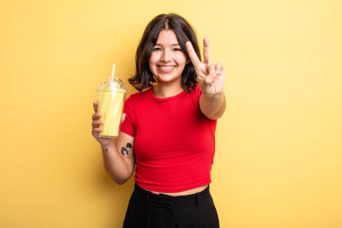 Genç, güzel bir bayan gülümsüyor ve iki numarayı gösteriyor. Milkshake konsepti