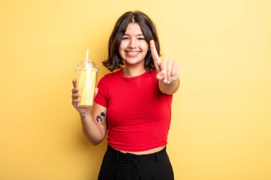 Genç, güzel bir bayan gülümsüyor ve arkadaş canlısı görünüyor. Bir numarayı gösteriyor. Milkshake konsepti