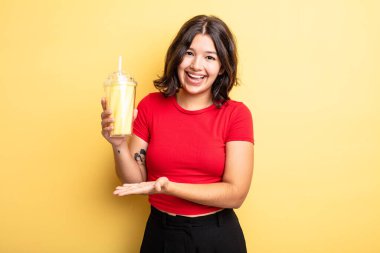 Genç, güzel bir kadın neşeyle gülümsüyor, mutlu hissediyor ve bir konsept gösteriyor. Milkshake konsepti