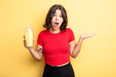 Genç ve güzel bir kadın şaşırmış ve şok olmuş görünüyor. Çenesi düşmüş ve elinde bir nesne tutuyor. Milkshake konsepti