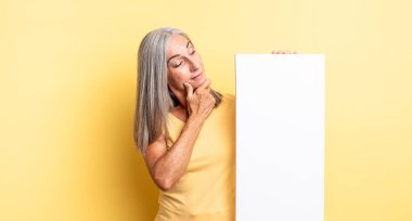 Orta yaşlı güzel bir kadın mutlu, kendinden emin ve elleri çenesinde gülümsüyor. boş tuval kavramı