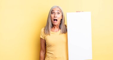 Orta yaşlı güzel bir kadın çok şaşırmış ya da şaşkın görünüyor. boş tuval kavramı