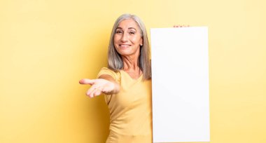 Orta yaşlı, güzel bir kadın arkadaşça gülümsüyor ve bir konsept sunuyor. boş tuval kavramı