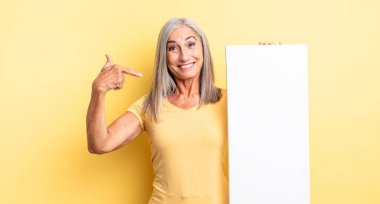 Orta yaşlı, güzel bir kadın kendini mutlu hissediyor ve heyecanla kendini işaret ediyor. boş tuval kavramı