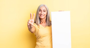 Orta yaşlı güzel bir kadın gülümsüyor ve arkadaş canlısı görünüyor. İki numarayı gösteriyor. boş tuval kavramı