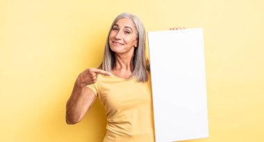 Orta yaşlı güzel bir kadın neşeli bir şekilde gülümsüyor, mutlu hissediyor ve bir tarafı işaret ediyor. boş tuval kavramı