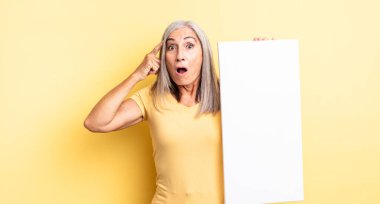 Orta yaşlı, güzel bir kadın şaşırmış görünüyor, yeni bir düşünce, fikir ya da konsept fark ediyor. boş tuval kavramı