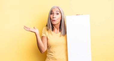 Orta yaşlı, güzel bir kadın şaşırmış ve şok olmuş görünüyor. Çenesi düşmüş ve elinde bir nesne var. boş tuval kavramı