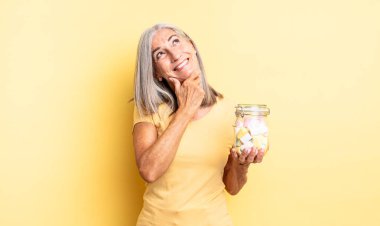 Orta yaşlı güzel bir kadın mutlu, kendinden emin ve elleri çenesinde gülümsüyor. Şeker şişesi konsepti