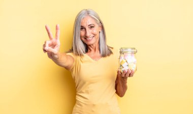 Orta yaşlı güzel bir kadın gülümsüyor ve mutlu görünüyor, zafer ya da barış işareti yapıyor. Şeker şişesi konsepti